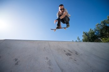 Skateboarder flying over a ramp on blue clear sky.