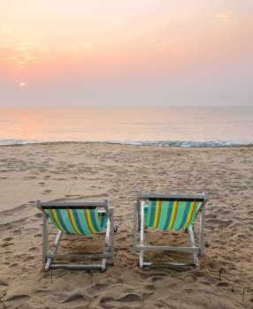 Two sun beach chairs on shore at sunrise in Thailand