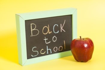 Back to School written on a chalkboard and red apple on yellow background