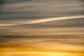 Abstract background of sky and clouds in horizontal streaks at sunset, glowing orange at bottom and dark at top.