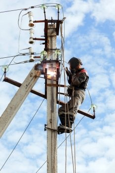 Electrician connects welding metal parts ground loop on a pole transmission line