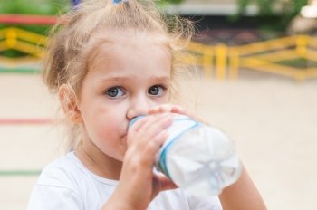 Three year old girl drinks from a bottle. Three year old girl drinks from a bottle at the playground