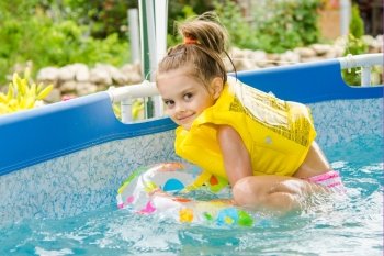 Cheerful girl bathing trying to get into the swimming circle. Six year old girl Europeans bathed in a small suburban pool