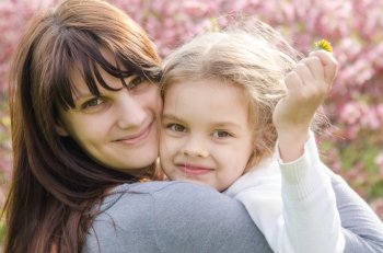 Portrait of mother and daughter on spring background. Portrait of a smiling mother and daughter in the spring blossoming background in sunny weather