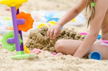 The girl builds a sand castle. Five-year girl on the bank of the river builds a sand castle