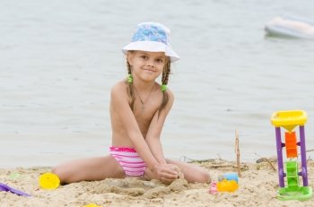 Five-year girl on a river in the sand beach Flashes. Funny five-year girl playing with sand molds on the beach