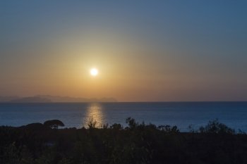 Sunset on the sea of sicily with trees.