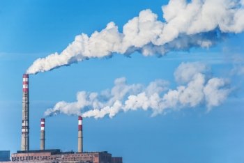 Factory chimneys with white smoke against a blue sky
