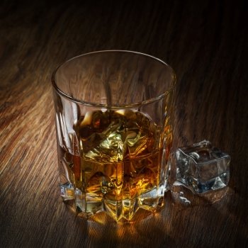Whiskey with ice in glass on the wood