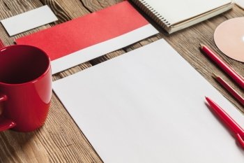 The mockup on wooden background with red calculator, pen, pencil, cup of coffee, white blank paper for writing, notebook and disk