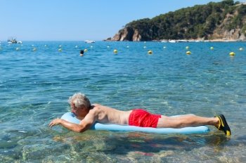 Retired man playing with inflatable bed floating in the sea