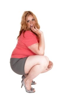 A lovely young plus size woman crouching on the floor, in gray shortsand high heels, isolated for white background..