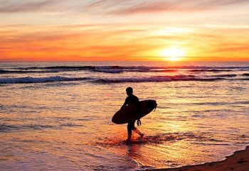 Silhouette of a surfer with surfboard on the beach at sunset. Portugal