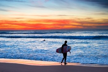 Surfer with surfboard walking on the beach at majestic sunset