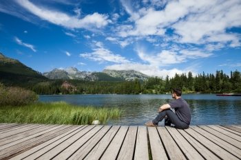 Man sitting on the bank of alpine mountain lake