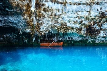 Wooden boat near steep rock on surface of underground lake (Melissani lake, Kefalonia, Greece).