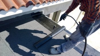 Roofer preparing part of bitumen roofing felt roll for melting by gas heater torch flame