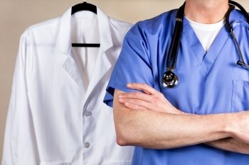 Close up partial view of medical doctor wearing scrubs and stethoscope with medical coat in background.