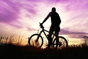 traveler with bike stopped on field at sunset time