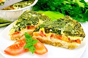 Two pieces of cake Celtic with spinach, tomatoes, oatmeal and eggs in a white plate in a baking dish from a foil on a wooden boards background