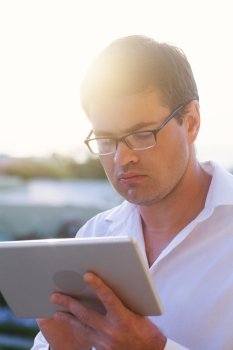 Young serious businessman in glasses using tablet computer outddor in bright sunshine