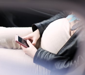 High-angle shot of pregnant woman sitting with smartphone in her hands.