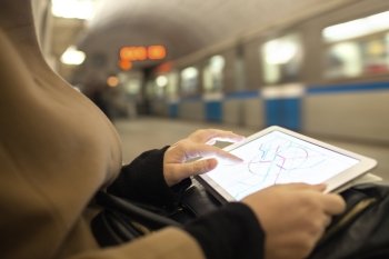 Close-up shot of woman using touch pad for searching on metro map being in underground. Blurred train in background. Tablet in female hands showing subway map in underground