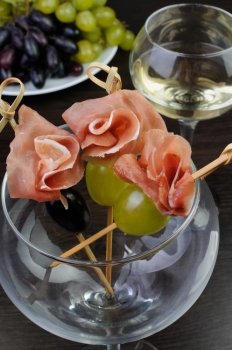 Appetizer of ham with grapes on a skewer in the glass