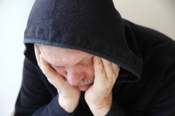 Senior man wearing a dark hoodie slumps in depression .