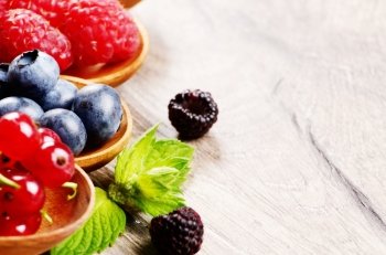 Spoons with berries on wooden table with copy-space