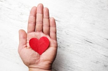 Heart in human hand. White wood background
