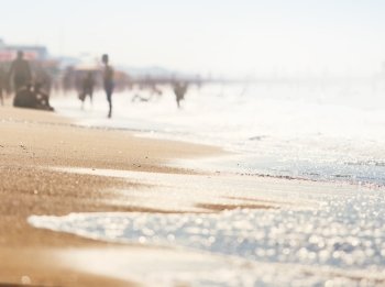 A wave thinning out of the sand of a beach, defocused people on the background