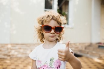 Cute little girl in red sunglasses showing a thumbs up 