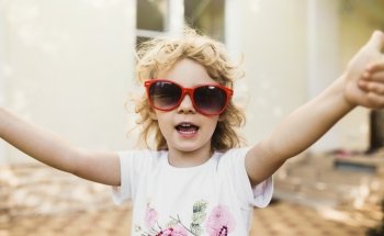 Cute little girl in red sunglasses showing a thumbs up 
