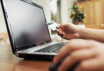 Man holding credit card in hand and entering security code using laptop keyboard 