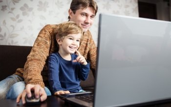 Father and son using laptop on sofa in house 