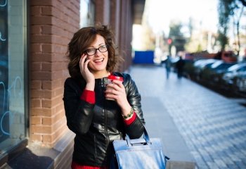 Modern young woman with coffee cup in hand talking on the mobile phone ,  urban background
