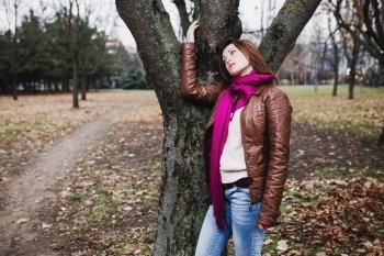 Pensive young  brunette girl standing near tree in autumn park