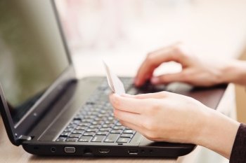 Close-up of woman holding credit card and using laptop