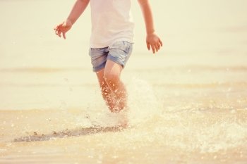 Child running beach shore splashing water, tinted photo