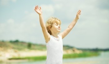 Happy child with raised arms standing near the sea. Vacation concept