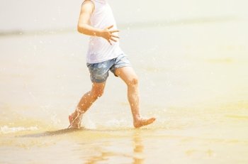 Child running beach shore splashing water, tinted photo