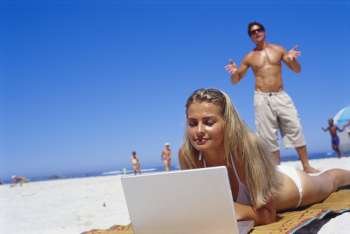 Young woman lying on the beach working on a laptop