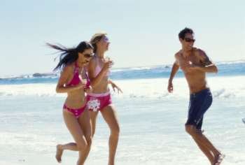 Two young women and a young man running on the beach