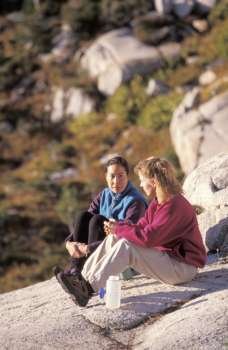 Two Female Hikers Sitting On A Rock And Resting Together
