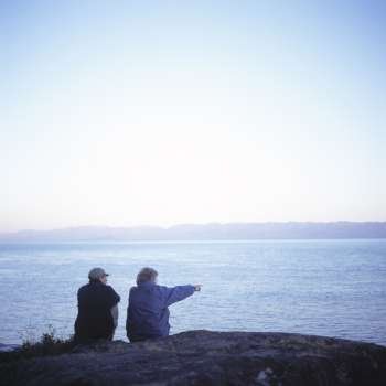 Elderly Couple Sitting On A Rock Overlooking The Sea