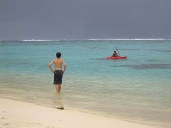 Rear of a young man standing on a beach watching a boat on the sea, Moorea, Tahiti, French Polynesia, South Pacific