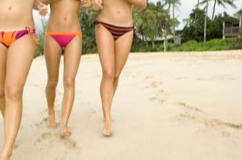 Low section view of three women walking on the beach