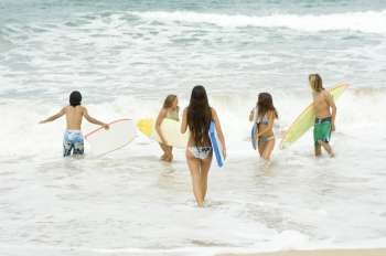 Three young women and two young men holding surfboard in the sea