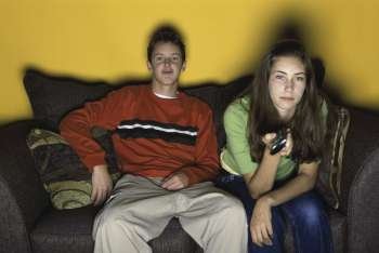 Teenage boy and a teenage girl sitting together on a couch watching television